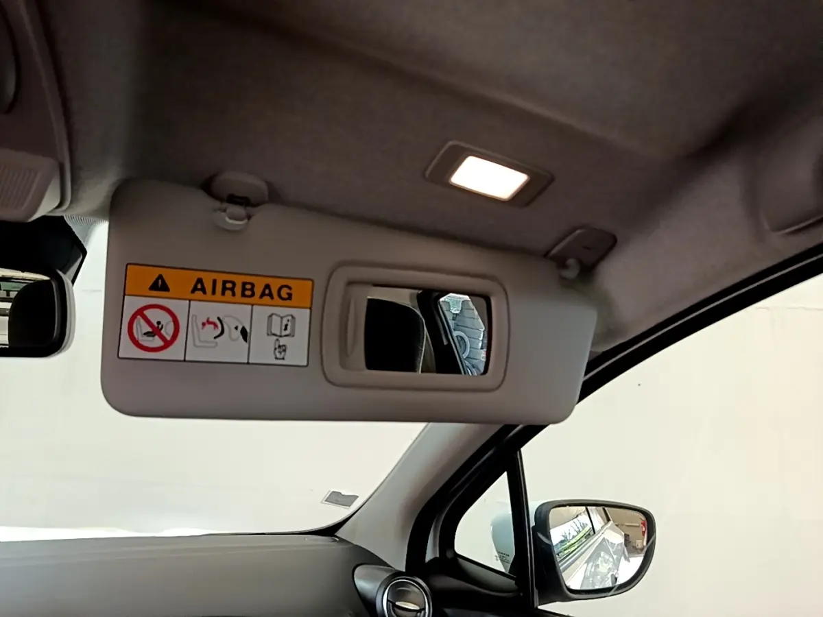 Vue intérieure du pare-soleil côté conducteur avec miroir et étiquette airbag, rétro extérieur visible, habitacle clair.