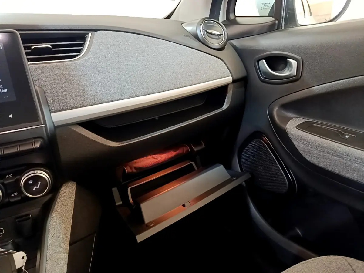 Vue intérieure côté passager de la Renault ZOE Zen R110 blanc, avec boîte à gants ouverte et tableau de bord gris.