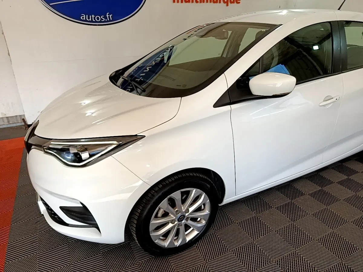 Vue 3/4 avant droit d'une Renault ZOE blanche 2019 avec phares LED et jantes alliage visibles.
