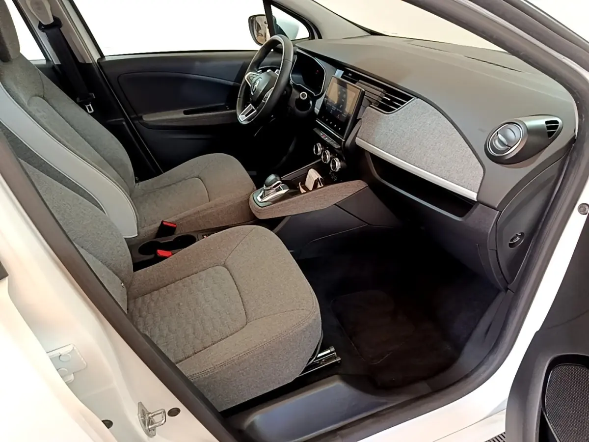 Intérieur avant droit de la Renault ZOE blanche, sièges tissu gris, tableau de bord avec écran tactile central.