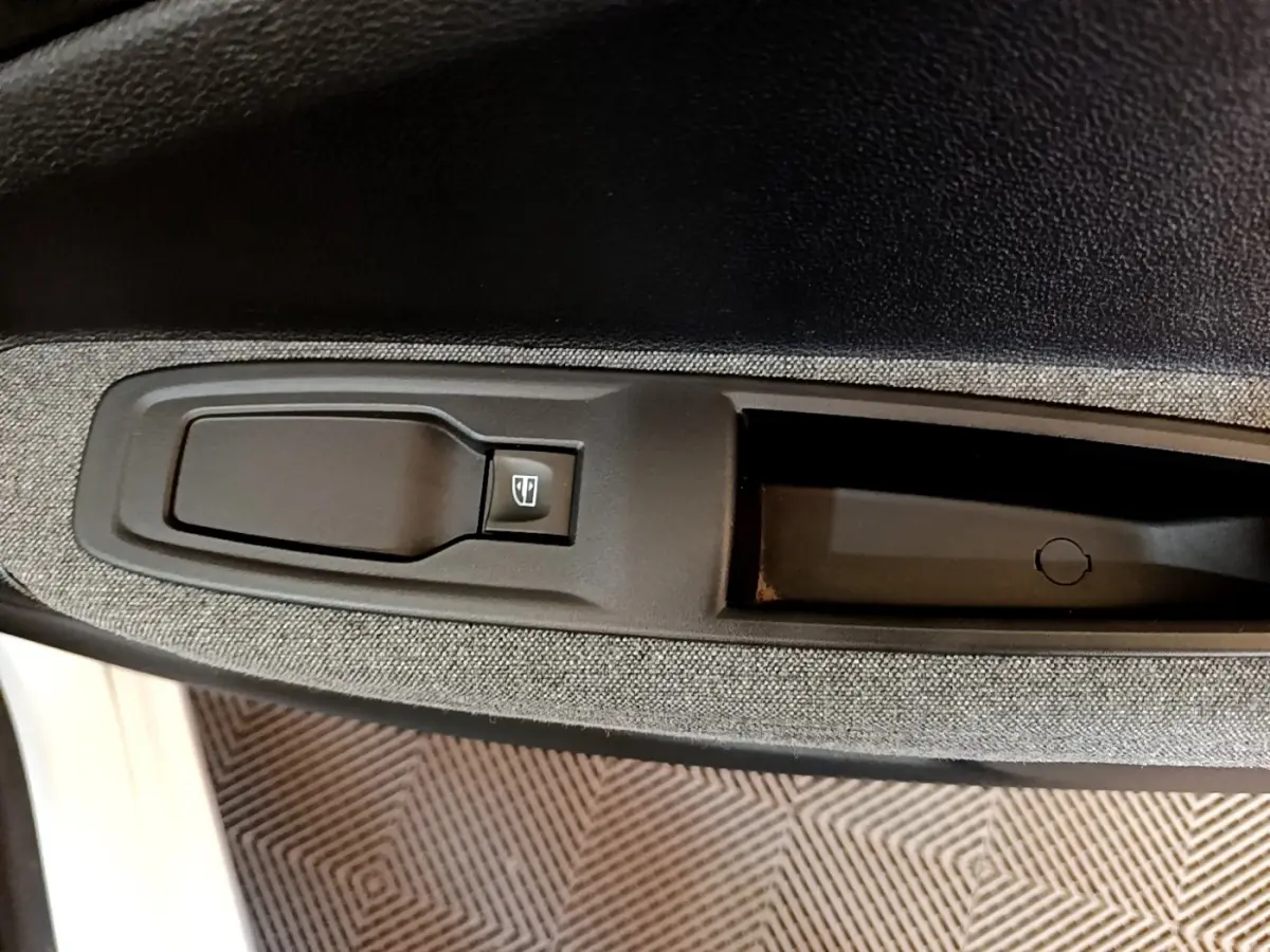 Gros plan sur la commande de lève-vitre côté conducteur de la Renault ZOE Zen R110 blanc, tissu gris sur la portière.