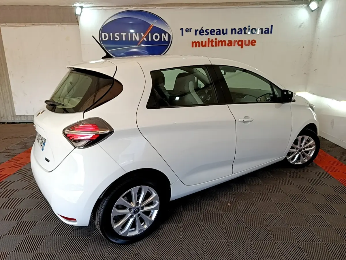 Vue 3/4 arrière droite d'une Renault ZOE Zen R110 blanche électrique, avec feux arrière LED et jantes alliage visibles.