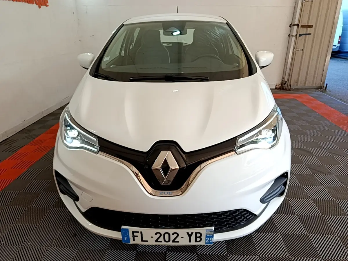 Vue avant d'une Renault ZOE blanche 2019 avec phares LED allumés et logo Renault bien visible.