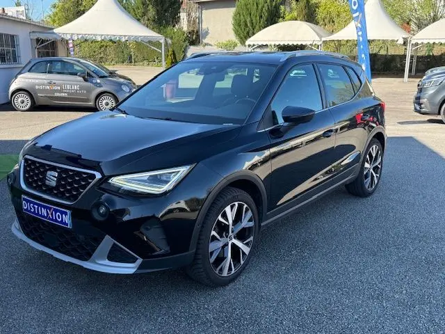 Vue 3/4 avant droite d'une SEAT Arona noire avec toit gris, jantes alliage 18'' et projecteurs LED allumés.