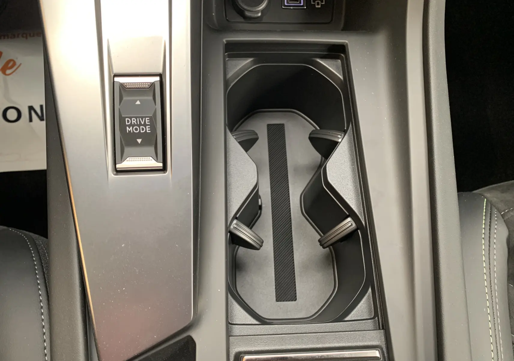 Vue rapprochée de la console centrale noire de la Peugeot 308 GT PHEV avec bouton Drive Mode et porte-gobelets.