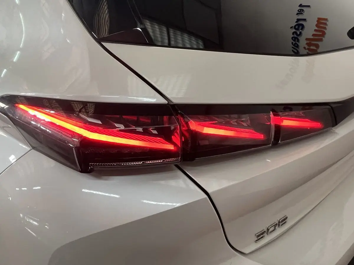 Gros plan sur le feu arrière droit allumé d’une Peugeot 308 GT PHEV blanc nacré, vue arrière détaillée.