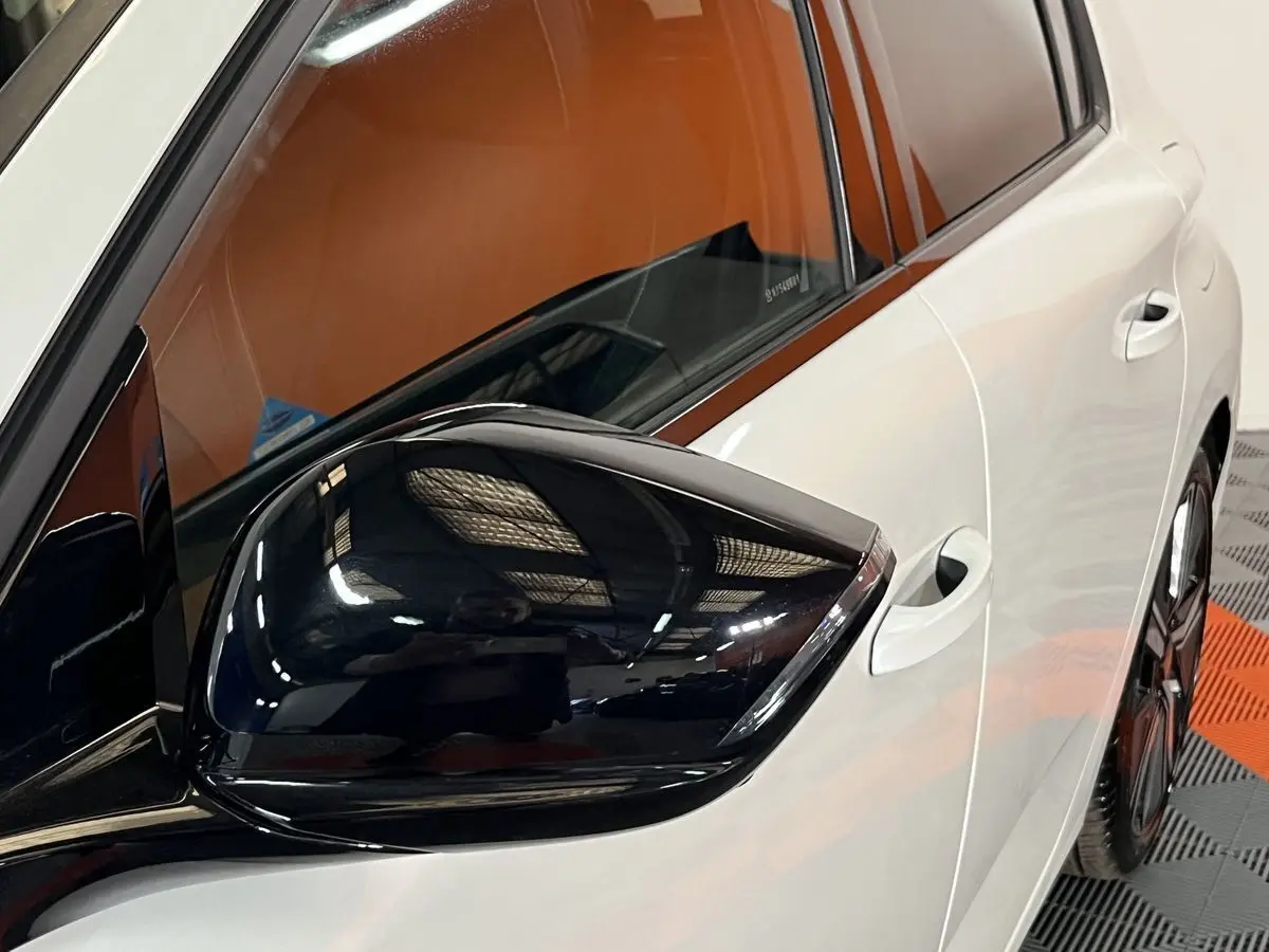 Vue rapprochée du rétroviseur noir côté gauche sur la porte blanche nacrée d’une Peugeot 308 GT PHEV 2022.