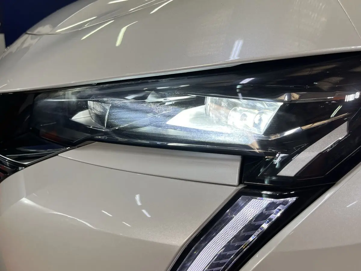 Gros plan sur le phare avant droit blanc nacré du Peugeot 308 GT PHEV 180 EAT8 avec éclairage LED allumé.