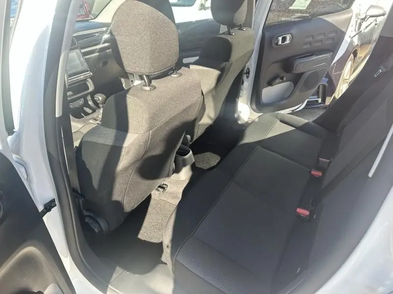 Vue intérieure arrière côté gauche d'une Citroën C3 blanche avec toit rouge, sièges noirs et porte arrière ouverte.