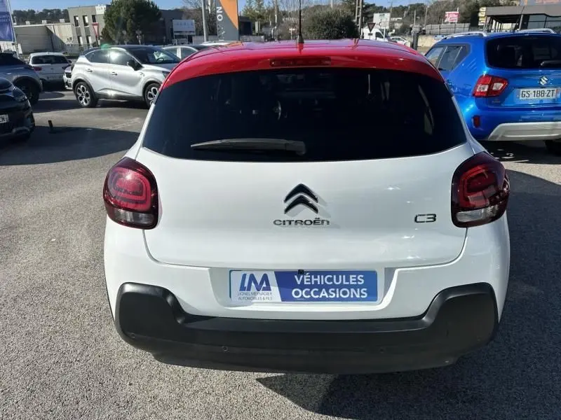 Vue arrière d'une Citroën C3 blanche avec toit rouge, affichant les feux arrière et le logo Citroën.