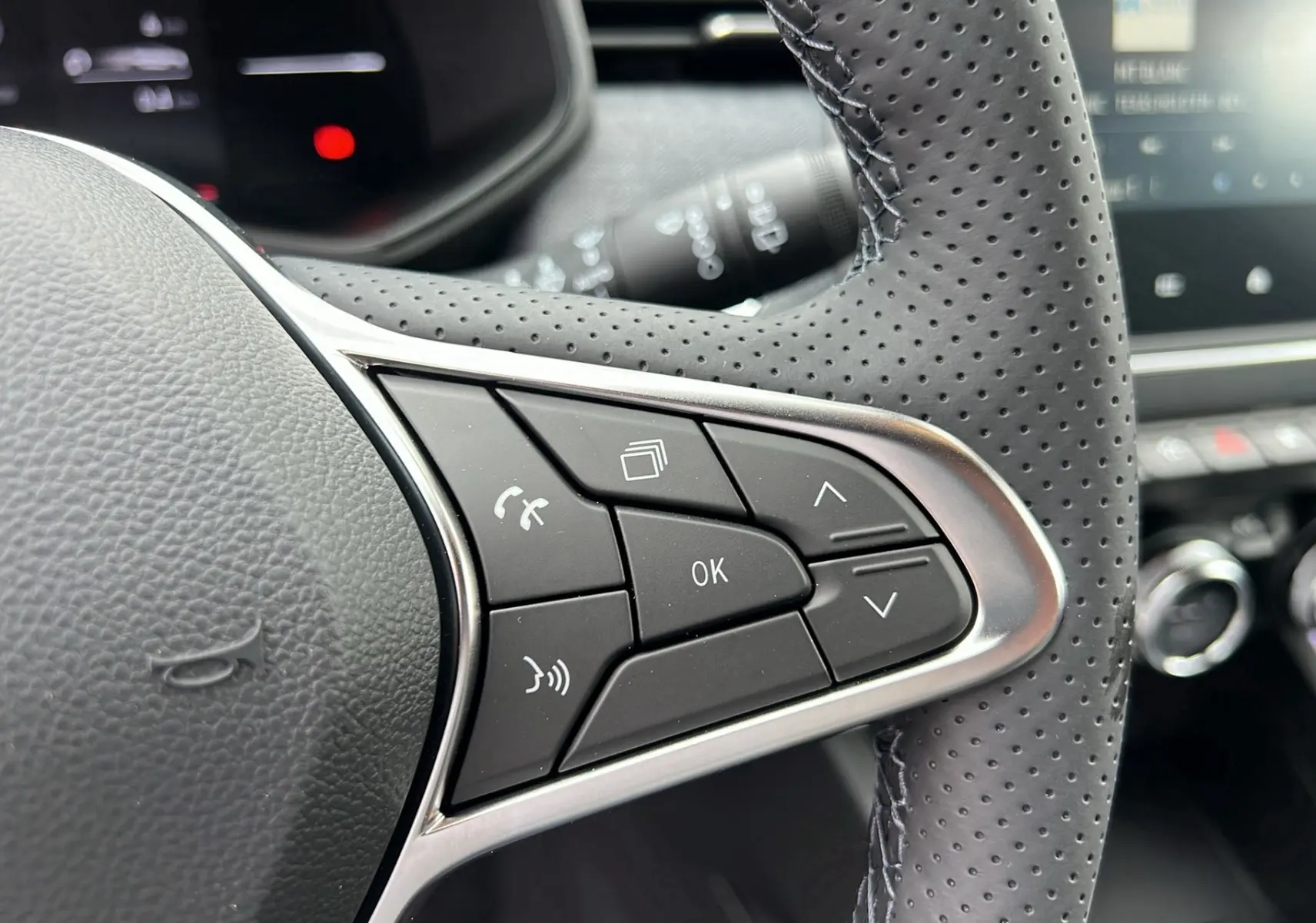 Gros plan sur les commandes multifonctions du volant perforé d'une Renault Clio gris schiste, version V TCE 90 TECHNO 2025.