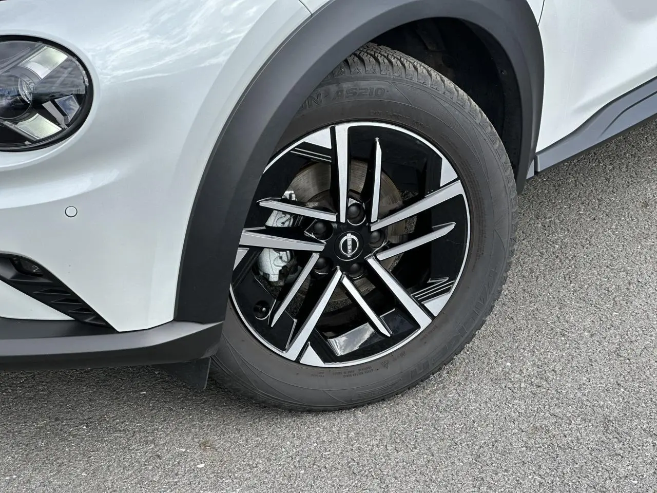 Gros plan sur la roue avant gauche du Nissan Juke blanc nacré, avec jante alliage noire et argentée design moderne.