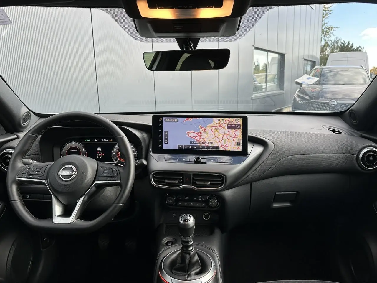 Vue intérieure frontale du tableau de bord noir du Nissan Juke blanc nacré avec écran tactile et levier de vitesse manuel.