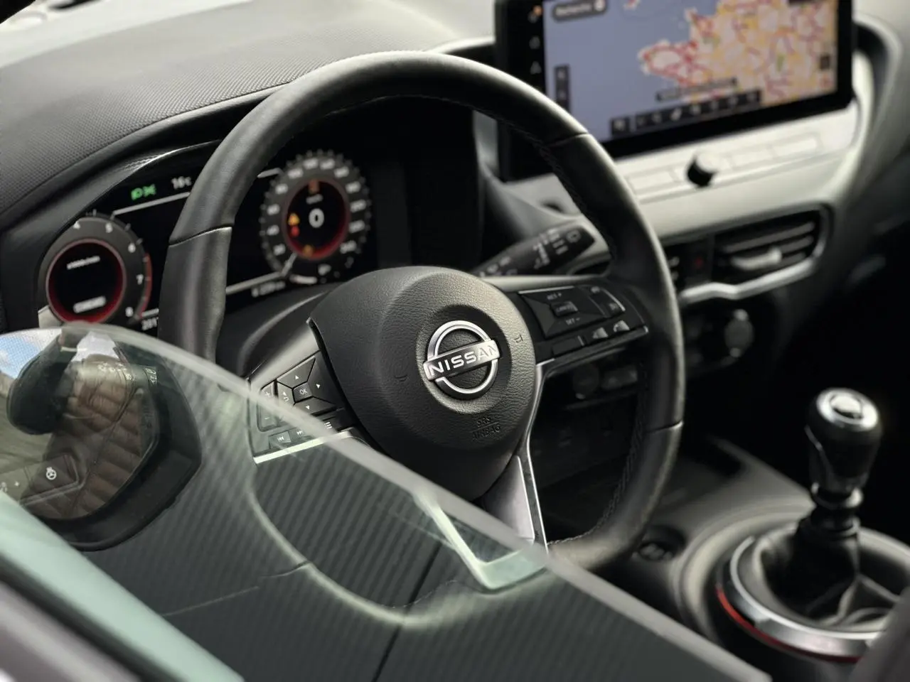 Vue rapprochée de l'intérieur du Nissan Juke 2025 montrant le volant cuir, la boîte manuelle et l'écran tactile central.