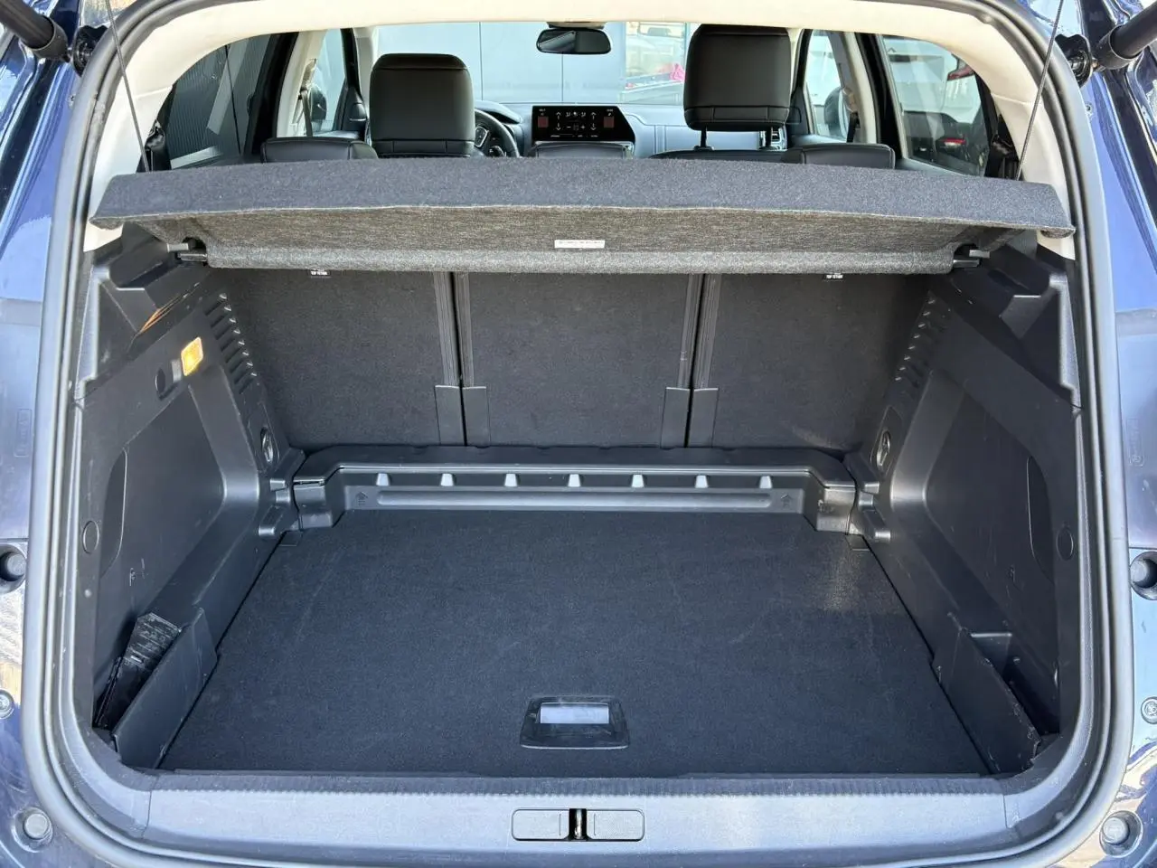 Coffre ouvert vu de l'arrière d'un Citroën C5 Aircross Hybrid bleu Eclipse, avec cache-bagages et sièges arrière visibles.