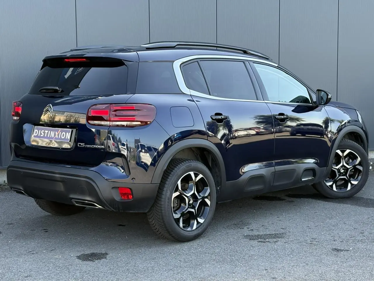 Vue 3/4 arrière droite du Citroën C5 Aircross bleu Eclipse avec jantes alliage bi-ton et barres de toit noires.