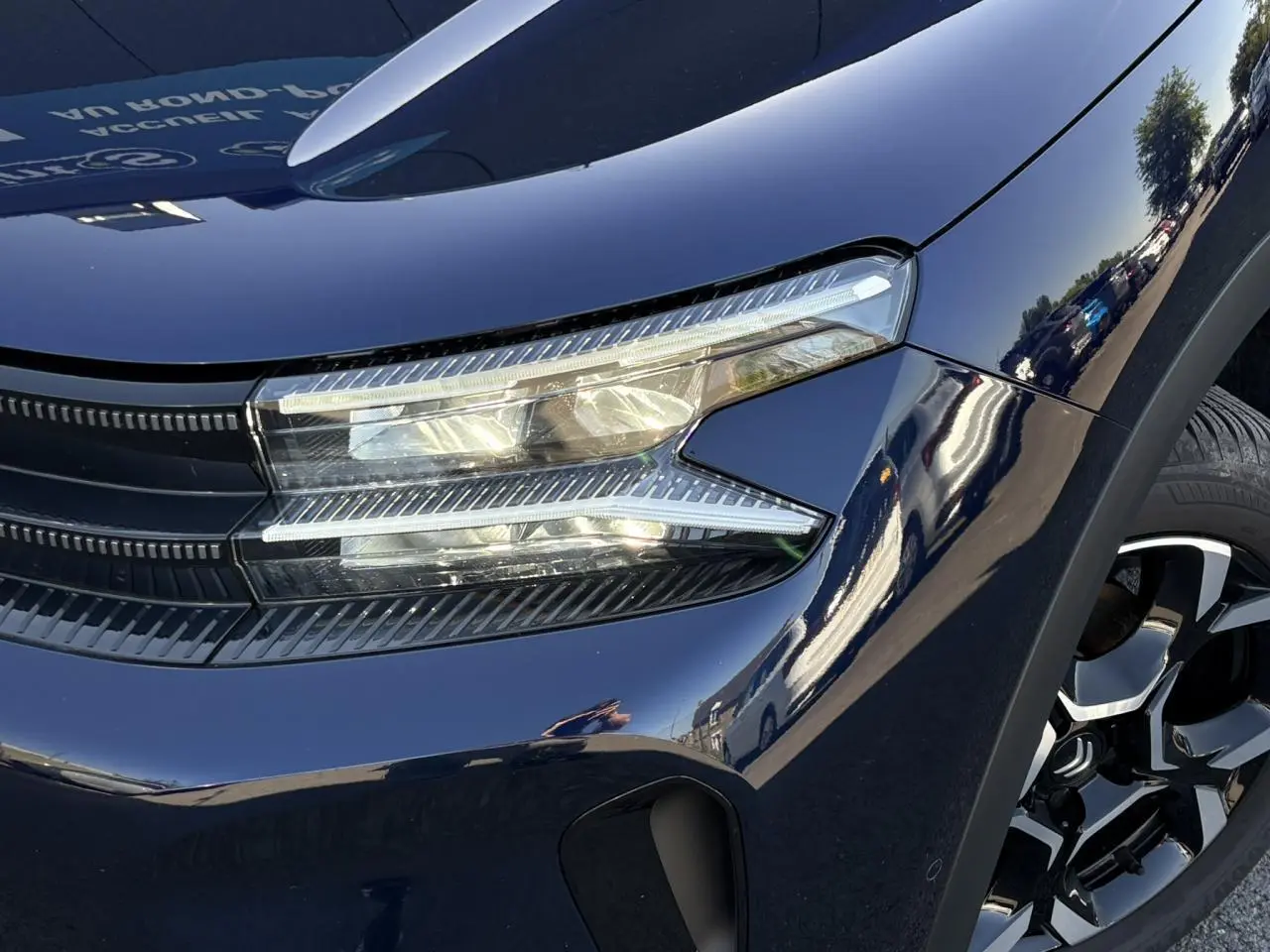 Gros plan sur l'avant droit bleu Eclipse du Citroën C5 Aircross 2025, mettant en valeur le phare LED et la jante alliage bi-ton.