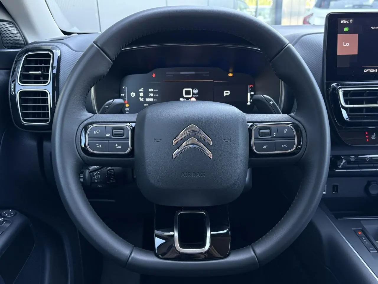 Vue rapprochée du volant noir de la Citroën C5 Aircross Hybrid 2025 avec commandes intégrées et tableau de bord numérique.