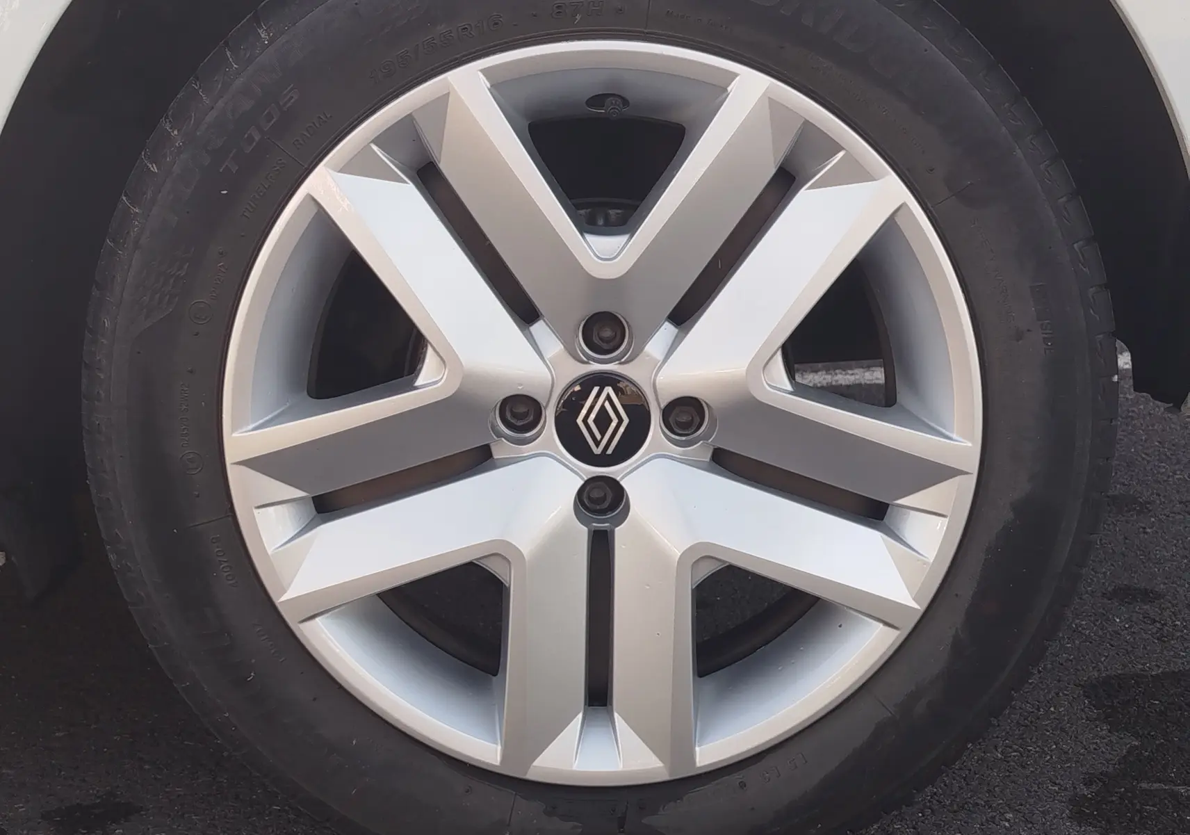 Gros plan sur la jante alliage argentée d’une Renault Clio blanche, mettant en valeur le logo Renault central.