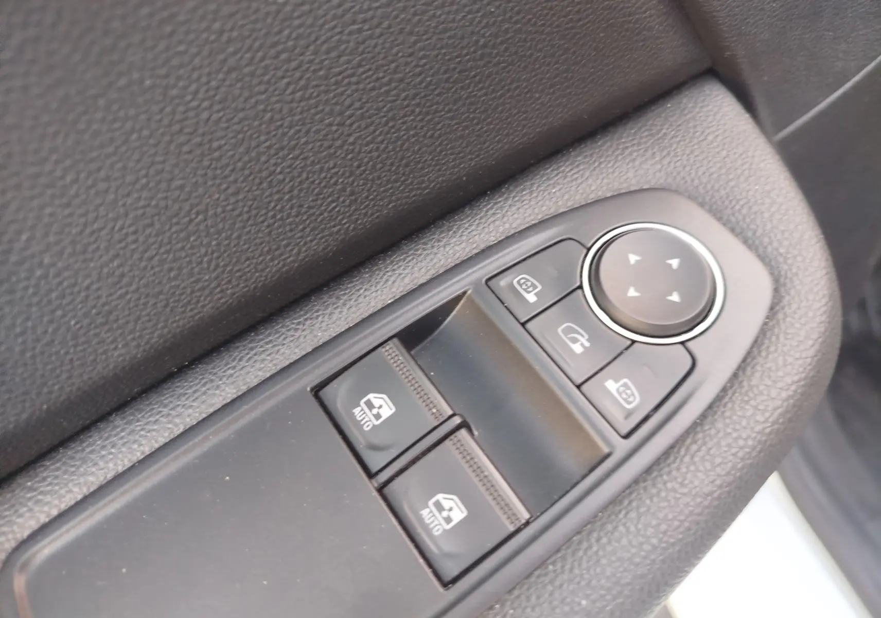 Gros plan sur les commandes des vitres électriques et rétroviseurs sur la porte intérieure côté conducteur d’une Renault Clio blanche.