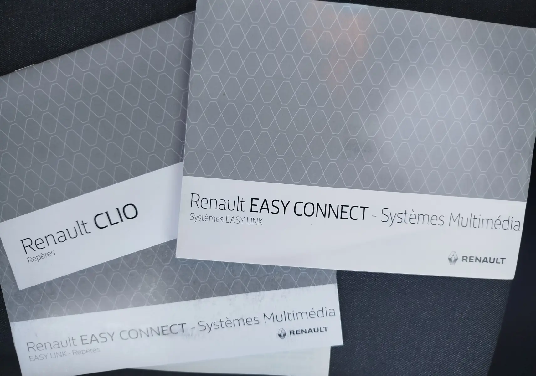 Image non conforme à la description d'un véhicule, montrant des brochures Renault Clio et Easy Connect posées sur un tissu sombre.