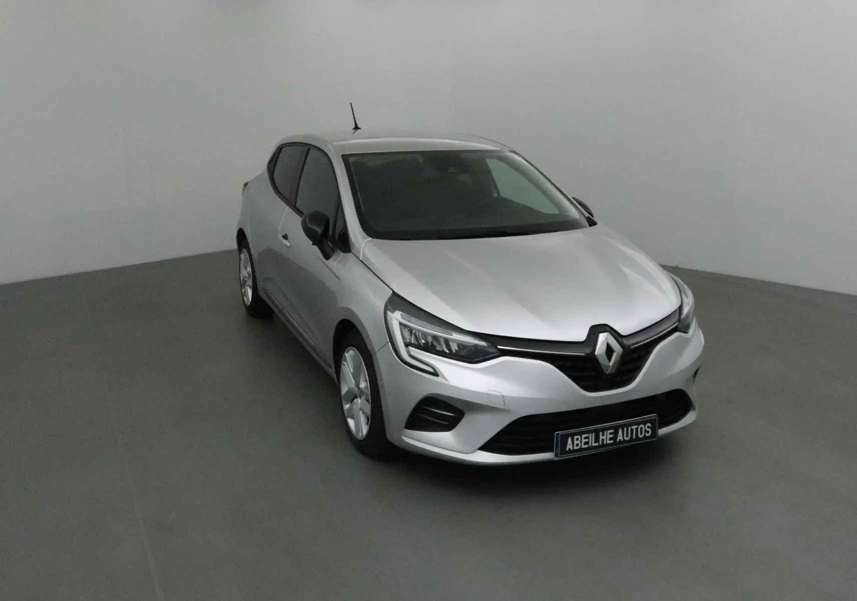 Renault Clio V gris platine vue 3/4 avant droit dans un studio, mettant en valeur ses optiques LED et calandre noire.