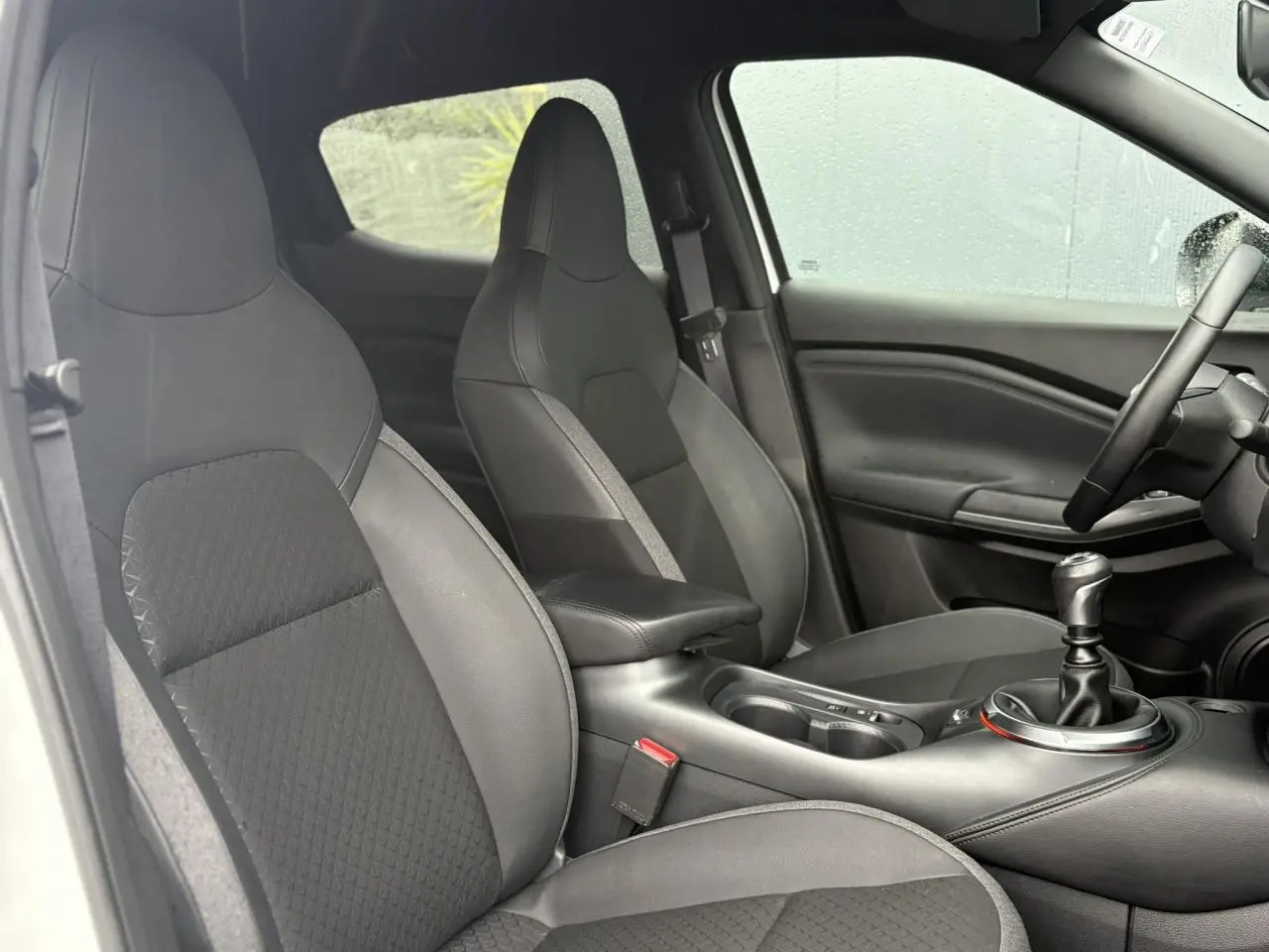 Vue intérieure côté conducteur du Nissan Juke 2025 avec sièges noirs et levier de vitesse manuel visible.