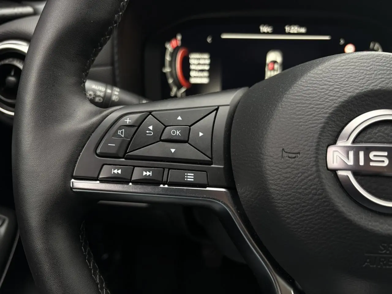 Gros plan sur le volant en cuir noir du Nissan Juke 2025 avec commandes multifonctions et tableau de bord digital flou.