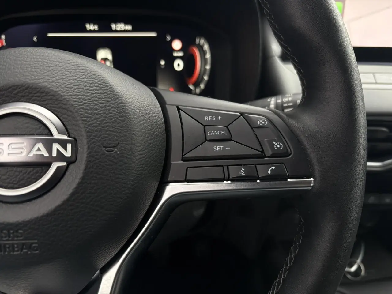 Gros plan sur le volant en cuir noir du Nissan Juke blanc nacré 2025, avec commandes intégrées au côté droit.