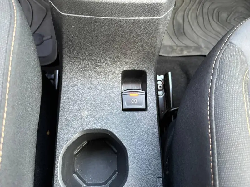 Gros plan sur la console centrale intérieure de la Dacia Sandero 2025 kaki, montrant le frein à main électrique et un porte-gobelet.