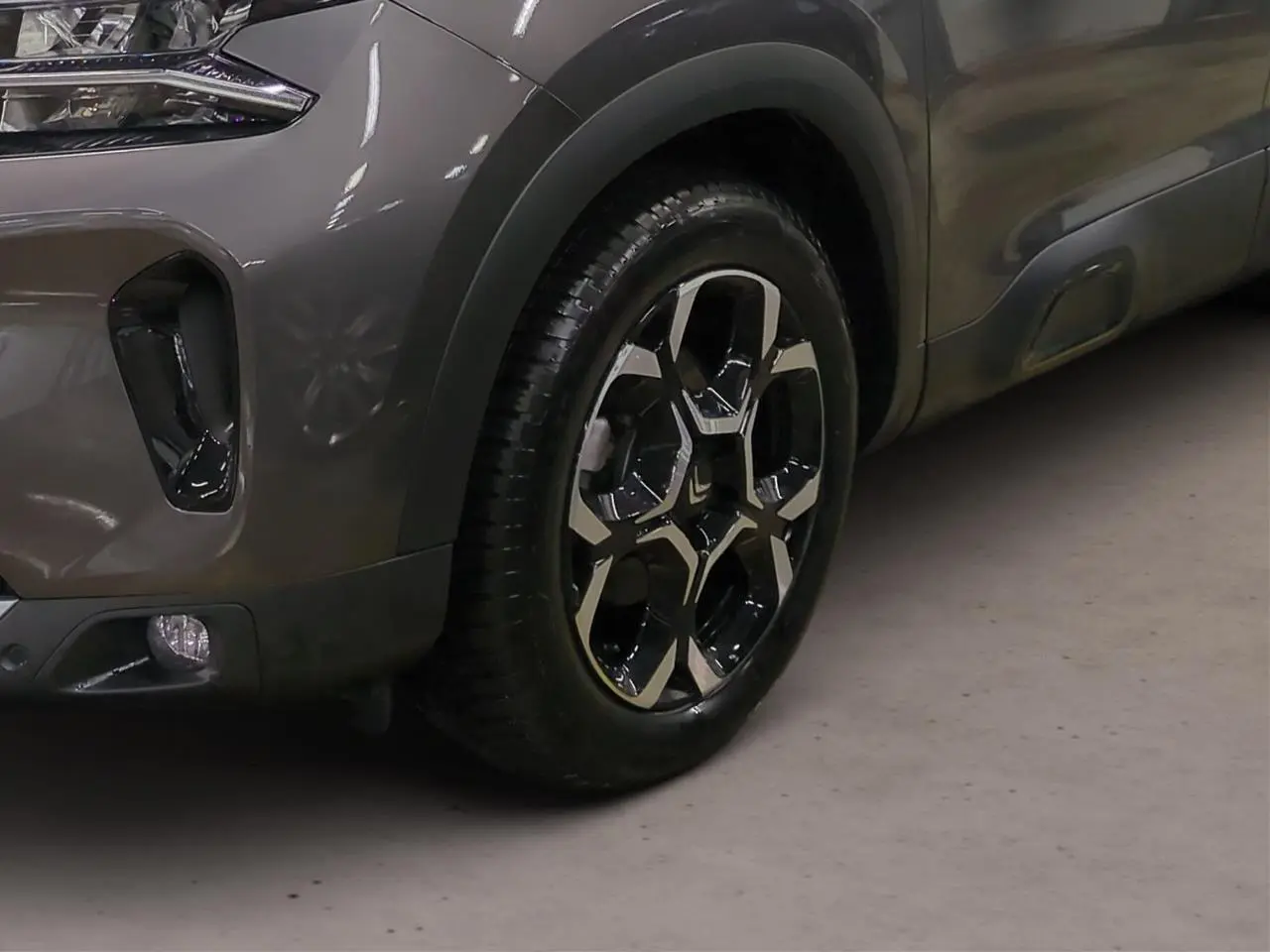 Gros plan sur la roue avant droite et la partie avant grise platinium du Citroën C5 Aircross Hybrid avec jante alliage bicolore.