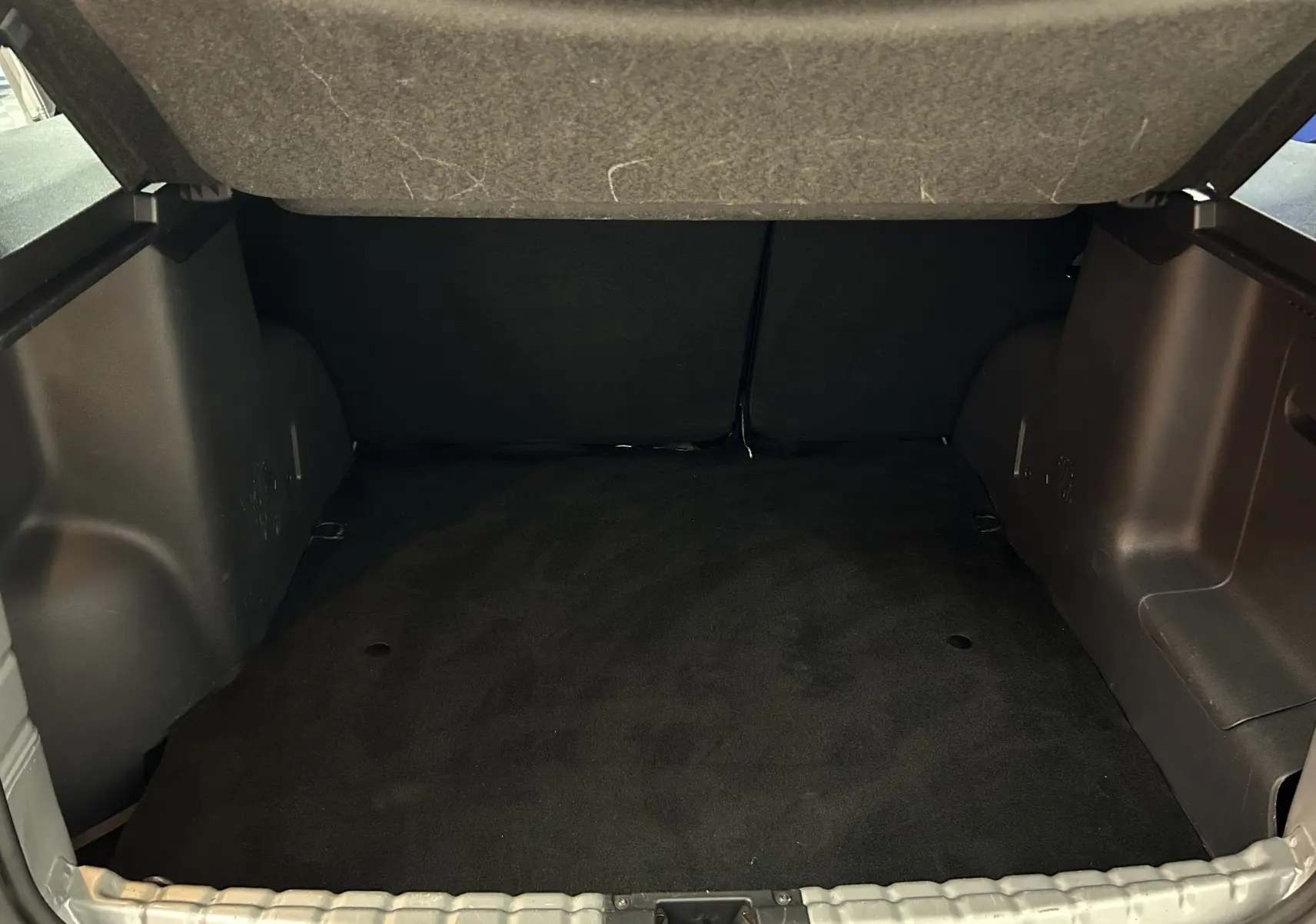Coffre ouvert du Dacia Duster gris 2017, montrant l'espace de chargement vide et la moquette noire.
