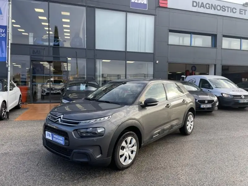 Citroën C4 Cactus gris foncé métal vue 3/4 avant droit, avec protections latérales caractéristiques, devant un garage.