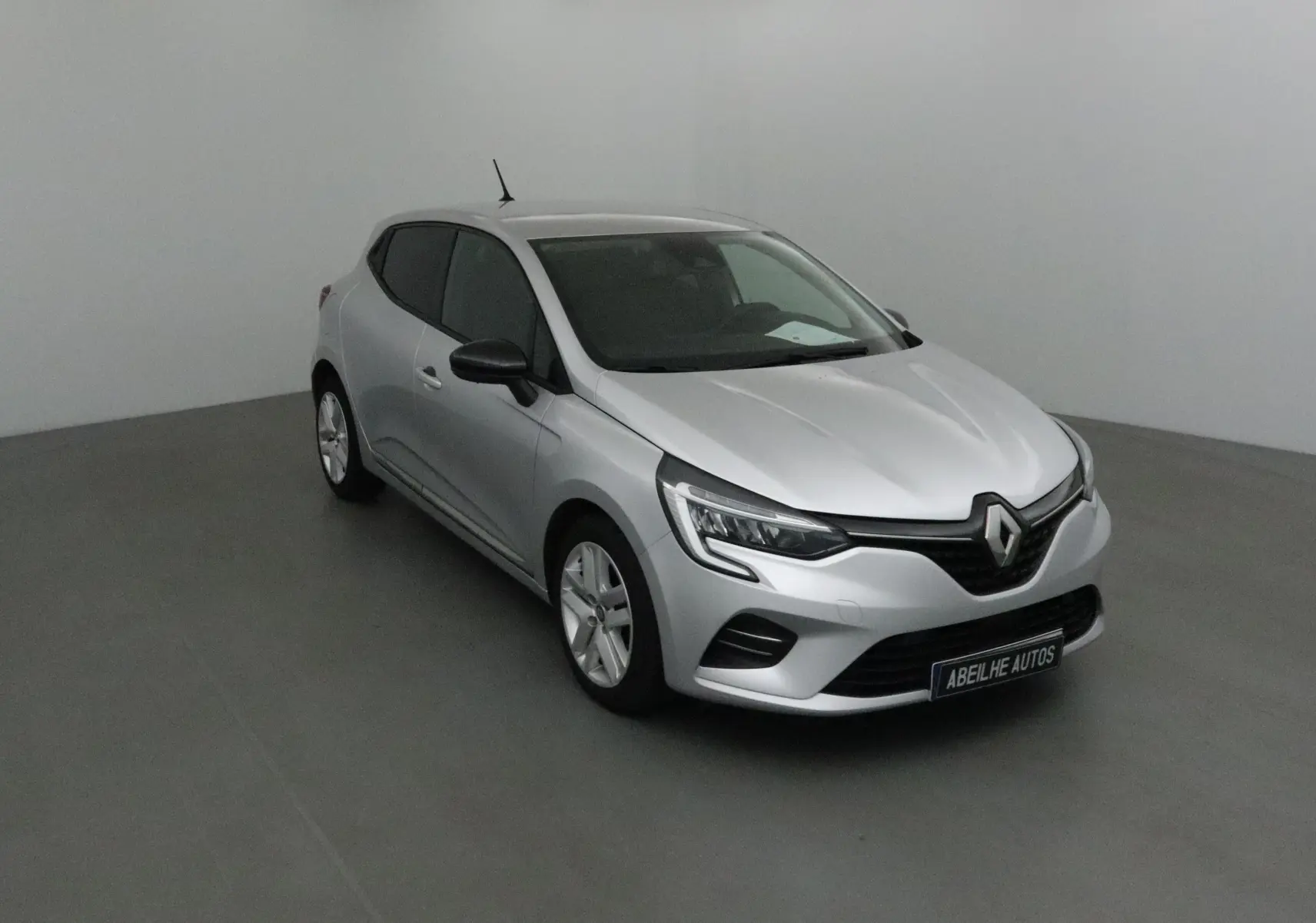 Renault Clio V gris platine vue 3/4 avant droit dans un studio avec phares LED et rétroviseurs noirs.