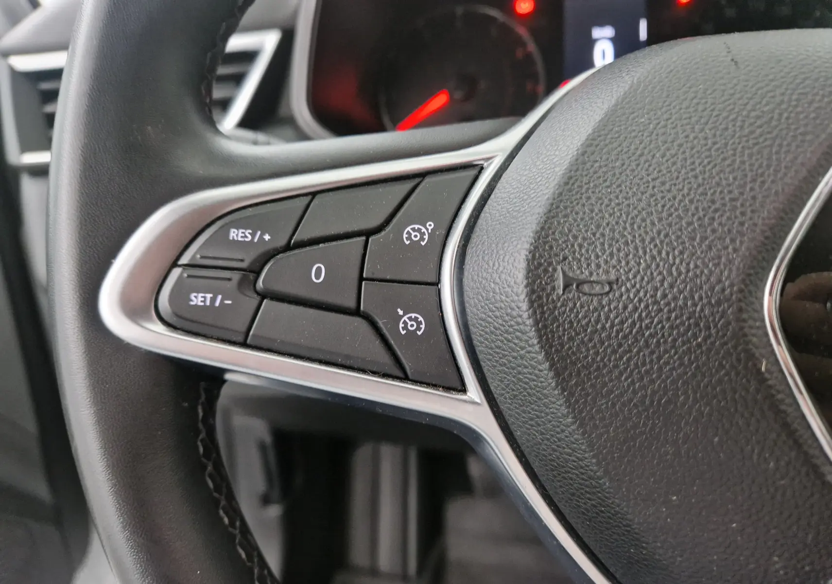 Gros plan sur les commandes de régulateur de vitesse à gauche du volant noir d'une Renault Clio V gris platine.