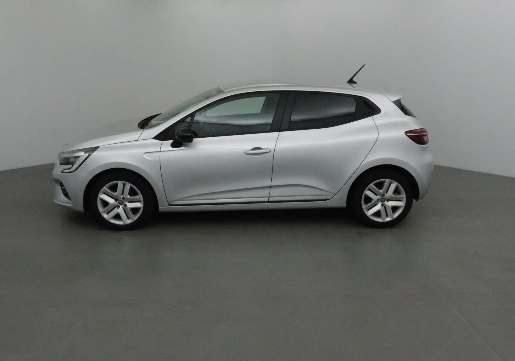 Profil côté gauche de la Renault Clio V gris platine 2021, compacte et élégante sur fond neutre intérieur.