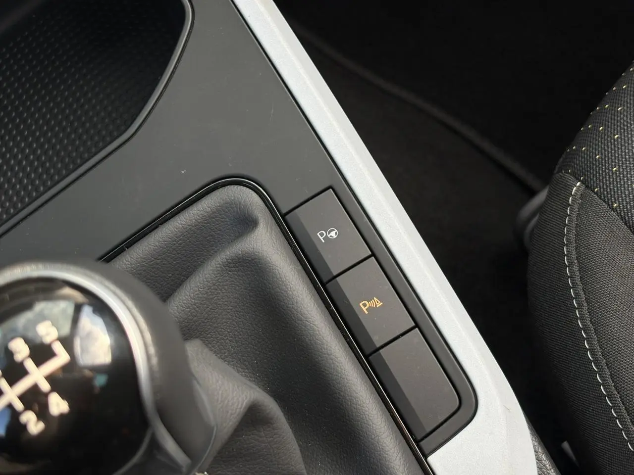 Gros plan sur la console centrale côté droit du SEAT Arona gris, avec levier de vitesse manuel et boutons d'aide au stationnement.