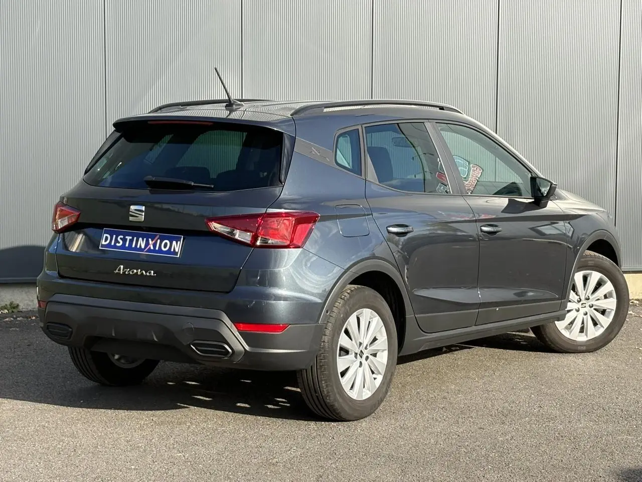 Vue 3/4 arrière droite d'un SEAT Arona gris magnétique 2024 avec barres de toit noires et jantes alliage 16 pouces.