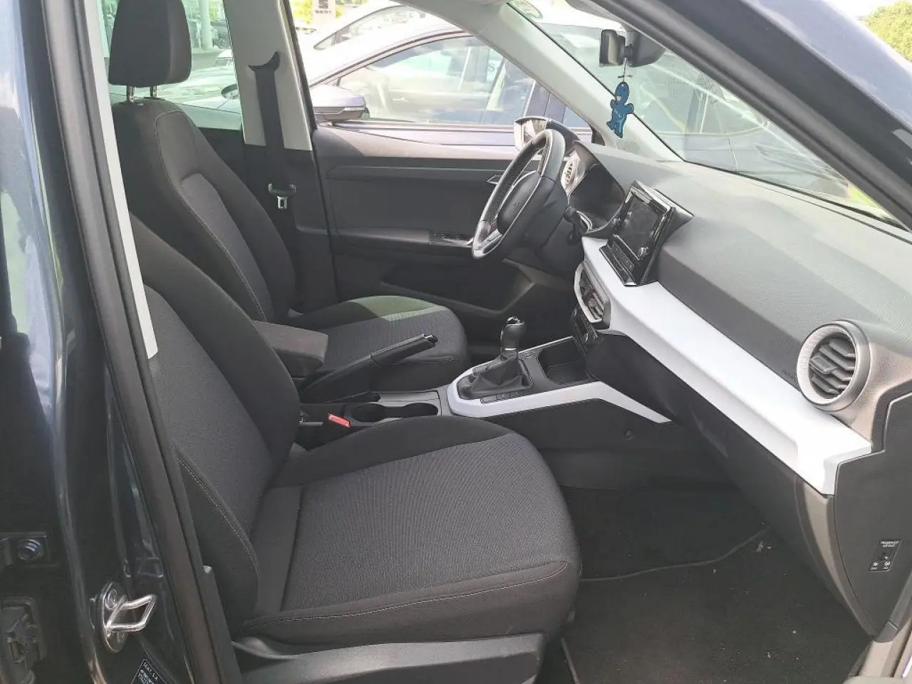Intérieur avant droit du SEAT Arona gris Magnétique 2024, montrant sièges tissu, volant multifonction et écran tactile central.