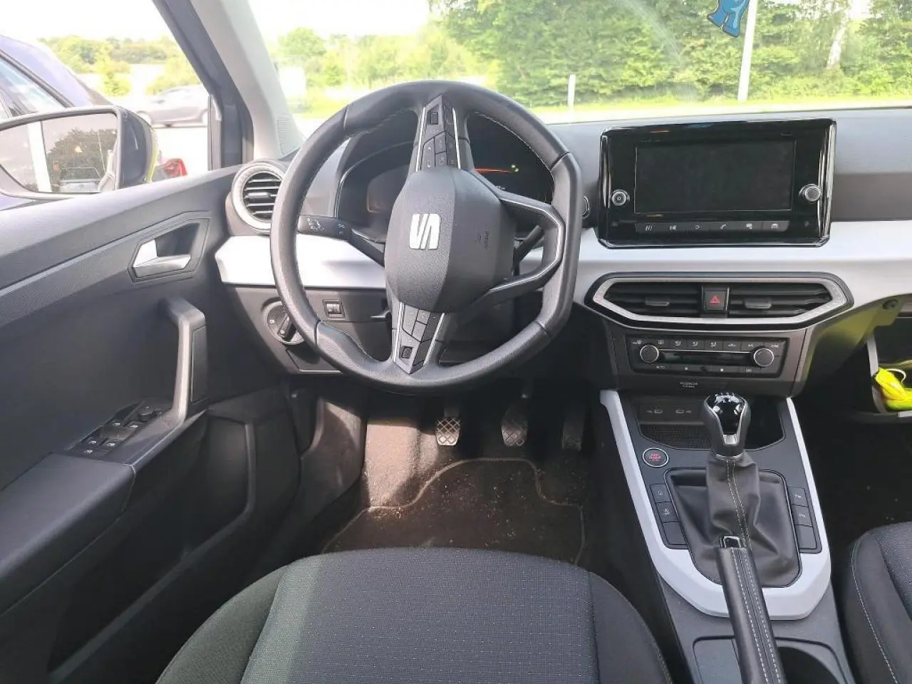 Intérieur du SEAT Arona 2024 vu de face, volant cuir multifonction, écran tactile et levier de vitesse manuel visibles.