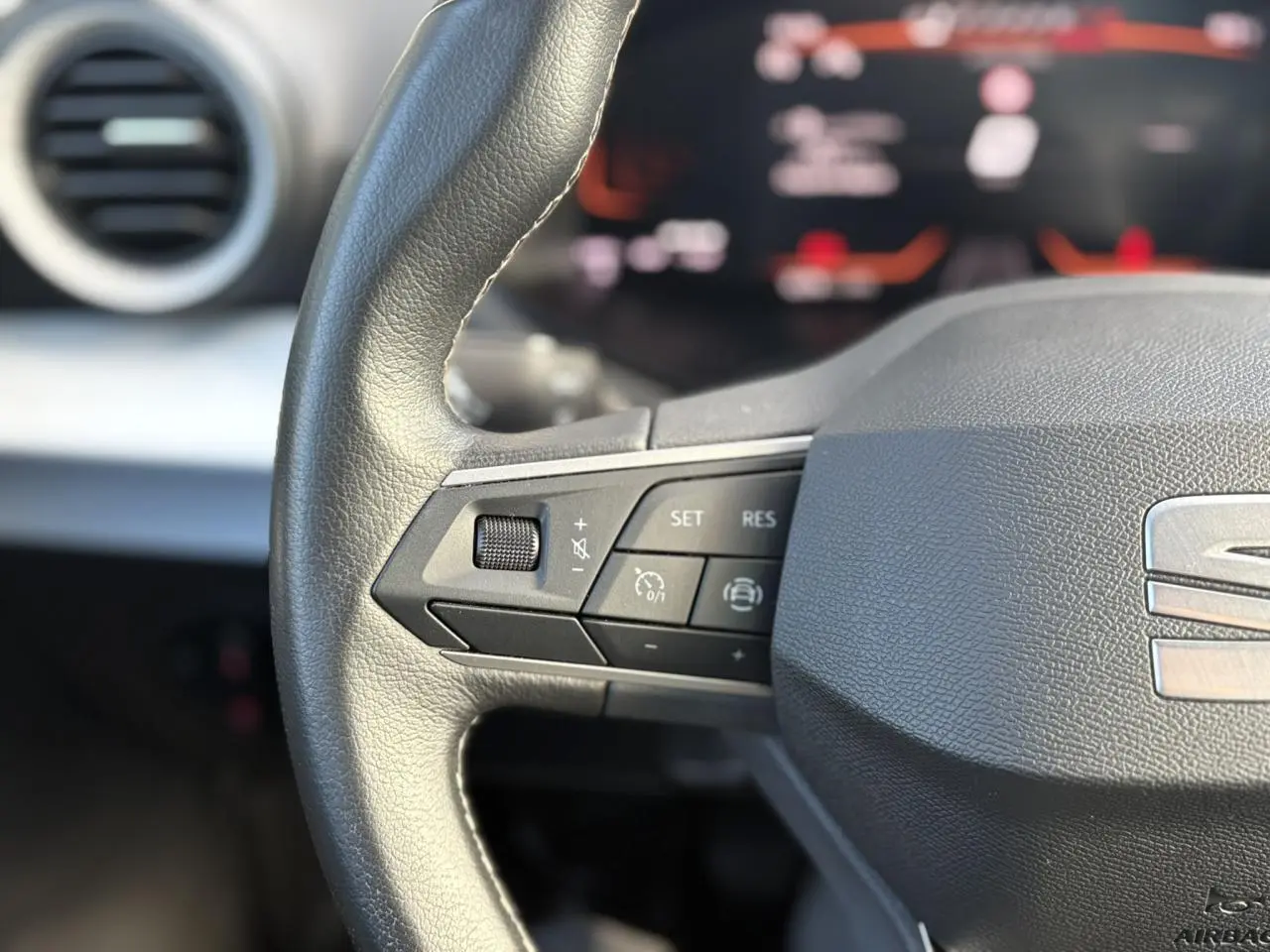 Gros plan sur le volant cuir multifonction gris du SEAT Arona 2024 avec commandes de régulateur et logo central visible.