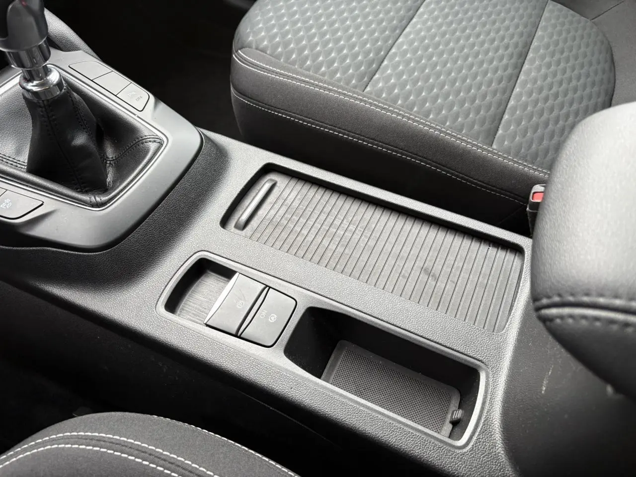 Gros plan sur la console centrale noire du Ford Kuga 2024 avec boîte manuelle et siège avant en tissu gris.