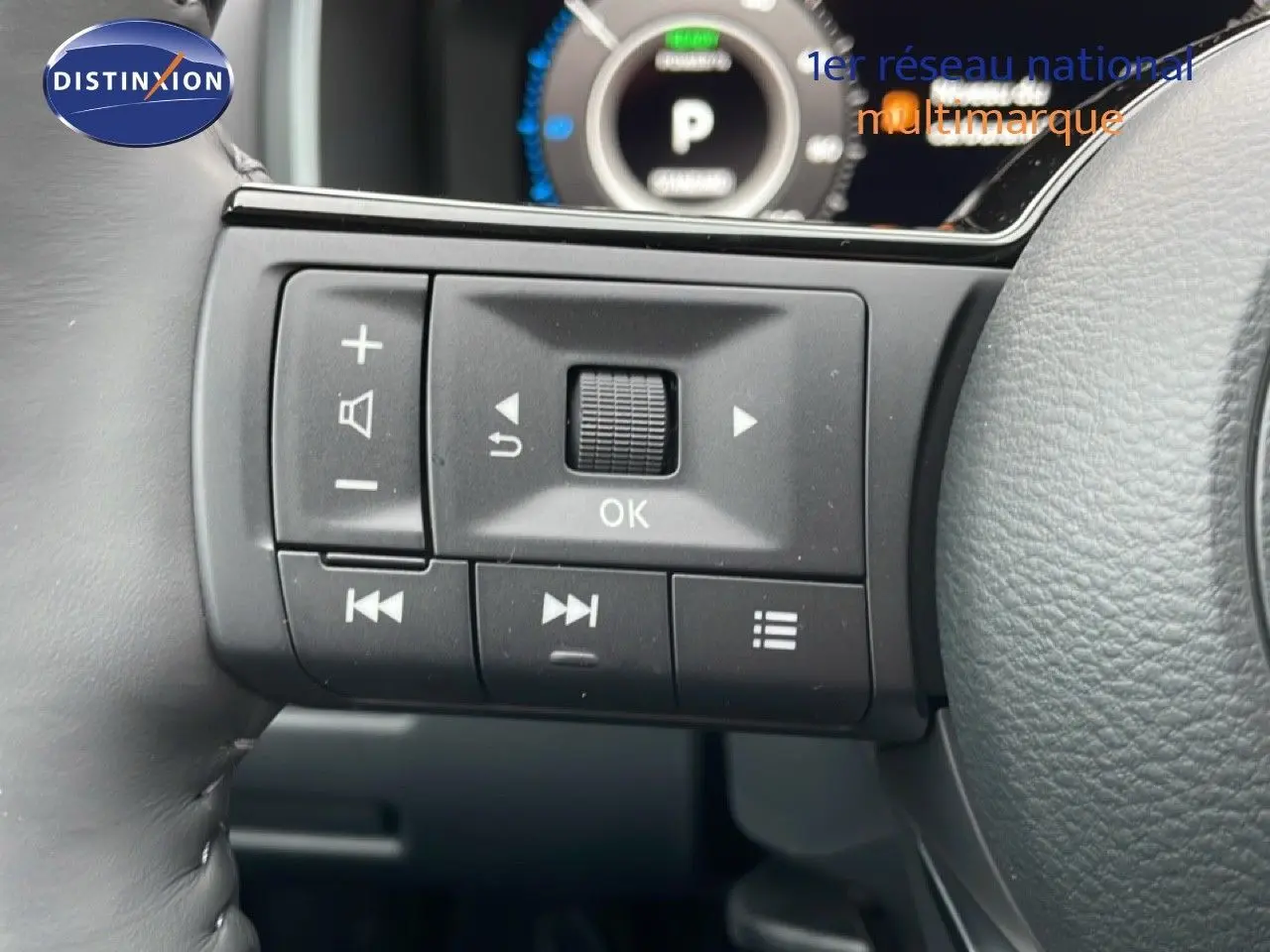 Gros plan sur les commandes au volant côté gauche du Nissan Qashqai blanc nacré 2025, affichage numérique en arrière-plan.