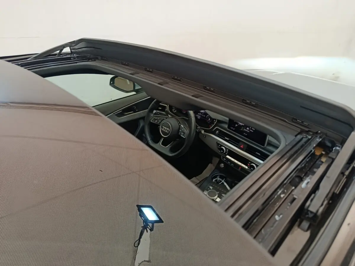 Vue intérieure par le toit ouvrant ouvert d'une Audi A5 gris clair, montrant le tableau de bord et le volant multifonctions.