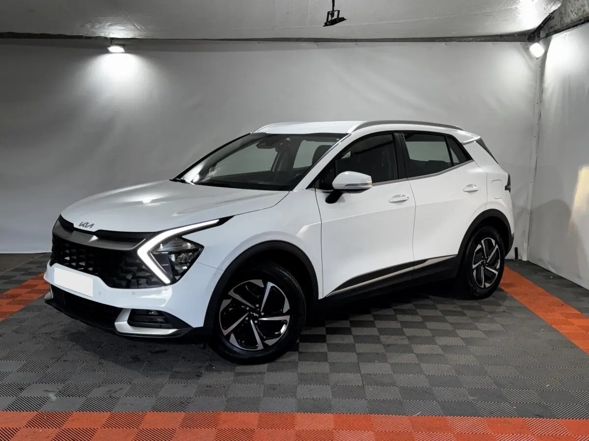 KIA Sportage blanc en 3/4 avant droit, avec signature lumineuse en forme de flèche et jantes noires distinctives.