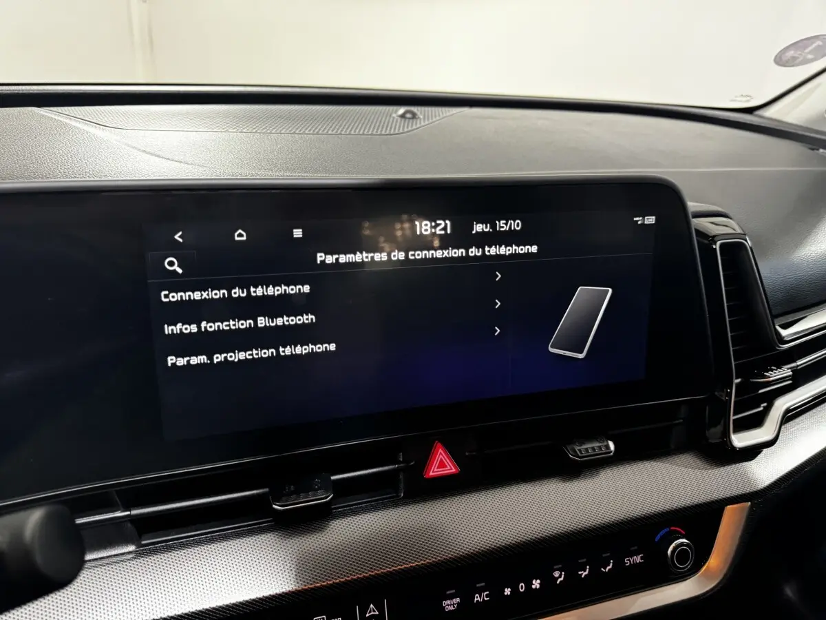 Gros plan sur l'écran tactile central du tableau de bord du Kia Sportage blanc 2024 affichant les paramètres de connexion téléphone.
