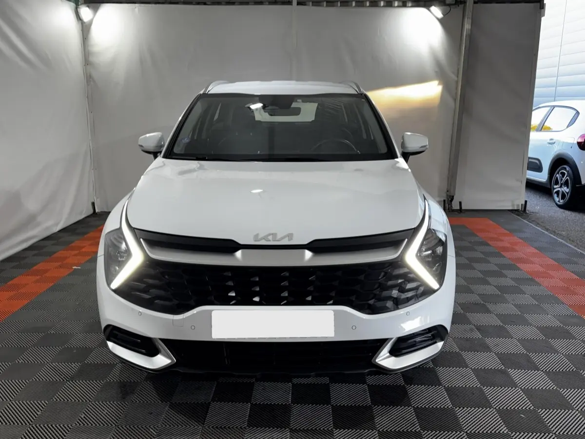 Vue frontale d'un Kia Sportage blanc 2024 avec feux diurnes LED en forme de flèche et calandre noire texturée.