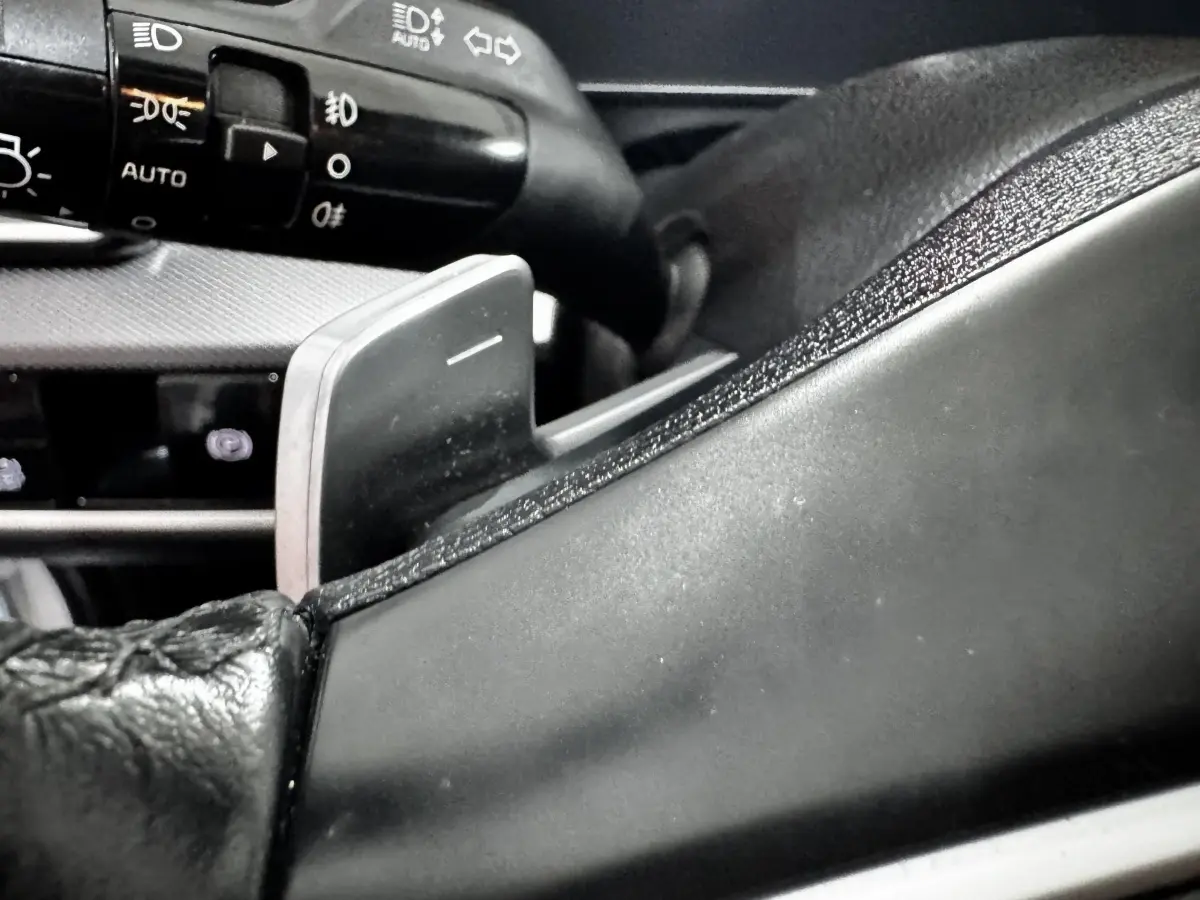 Gros plan sur la palette de changement de vitesse derrière le volant cuir du Kia Sportage 2024, intérieur noir.