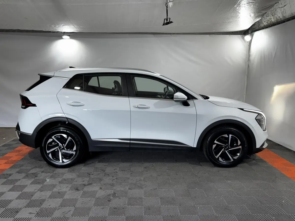 Profil droit d'un KIA Sportage blanc 2024 hybride essence, avec jantes noires et détails noirs contrastants.