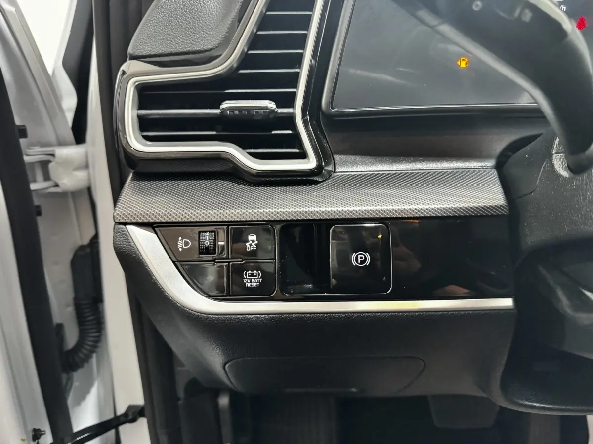 Détail du tableau de bord côté gauche du Kia Sportage blanc 2024 avec commandes d'éclairage et frein à main électrique.